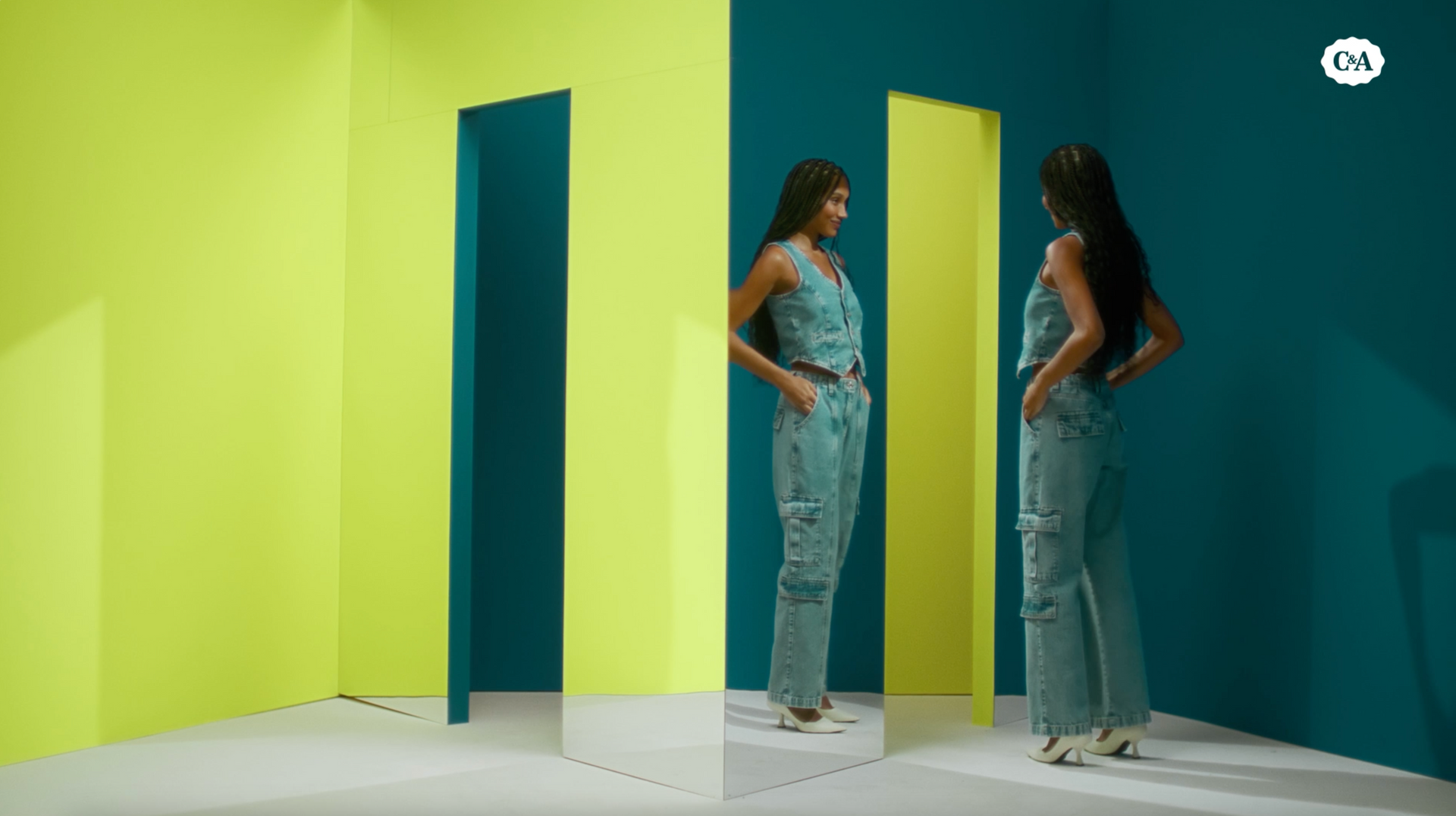 Uma mulher está diante de um espelho em uma sala com paredes verdes e amarelas.