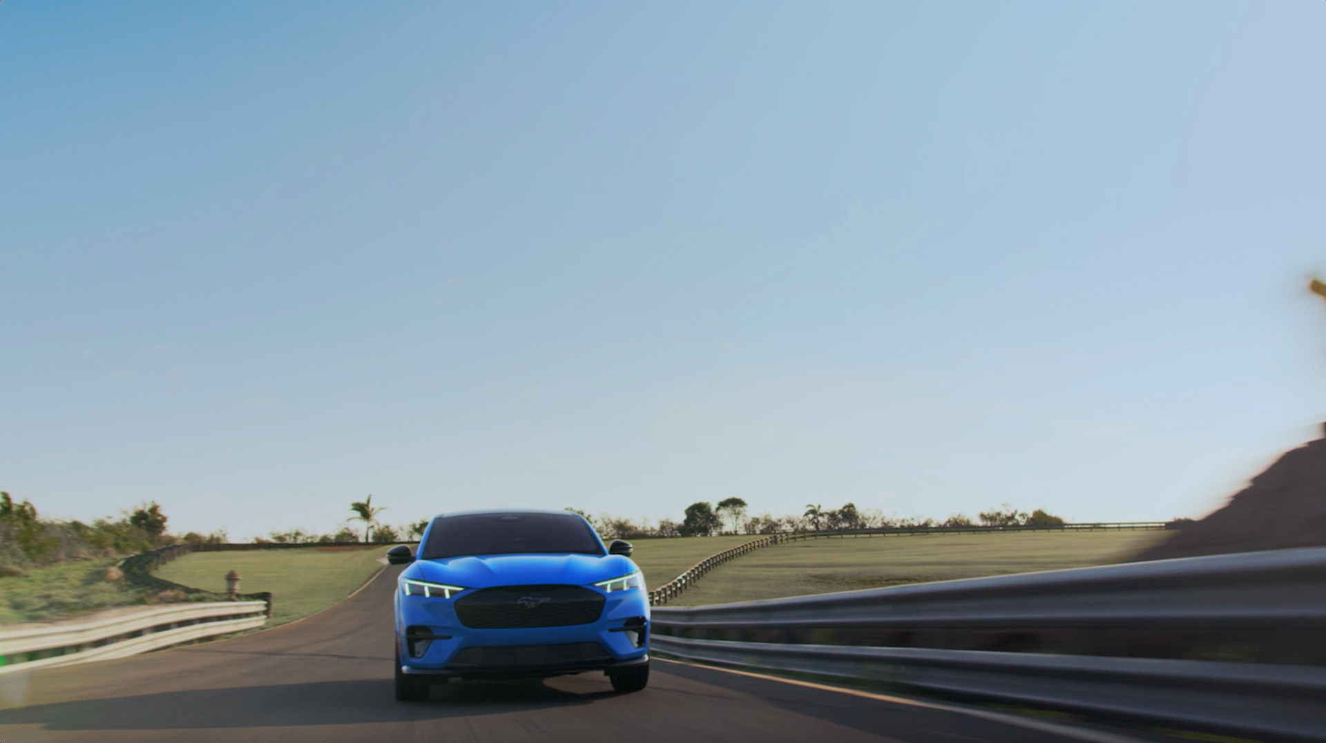 Um ford mustang mach e azul está dirigindo por uma estrada.