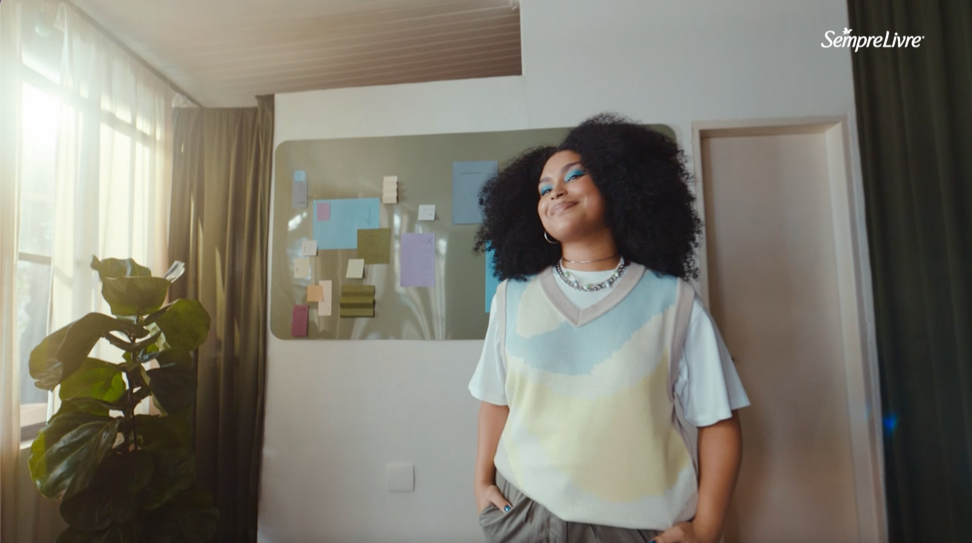 Uma mulher com cabelos cacheados está parada em uma sala de estar em frente a uma pintura.