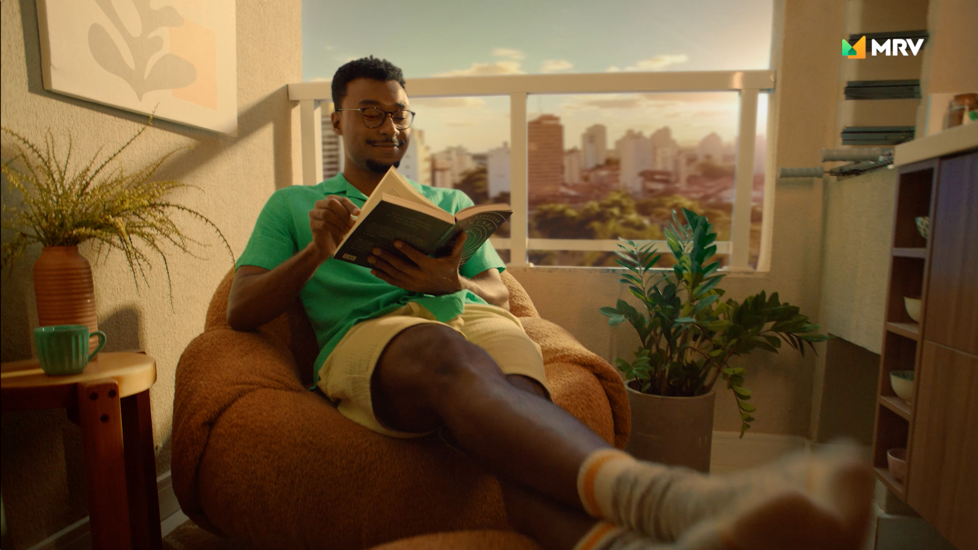 Um homem está sentado em um pufe lendo um livro.