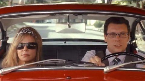 Um homem e uma mulher estão dirigindo um carro vermelho.