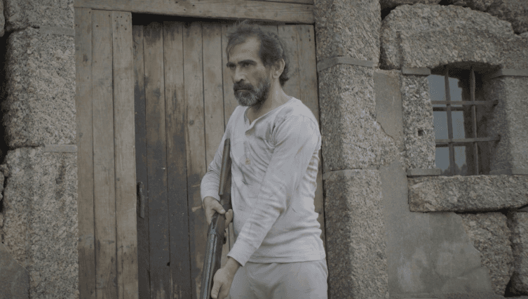 Um homem barbudo está parado em frente a uma porta de madeira.