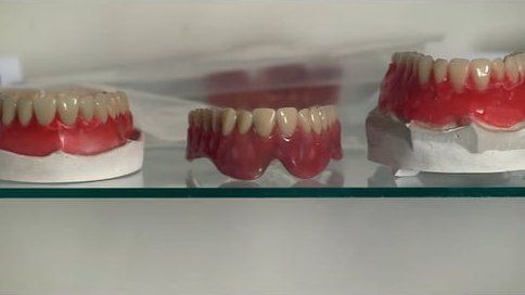 Três dentaduras estão em uma prateleira de vidro.
