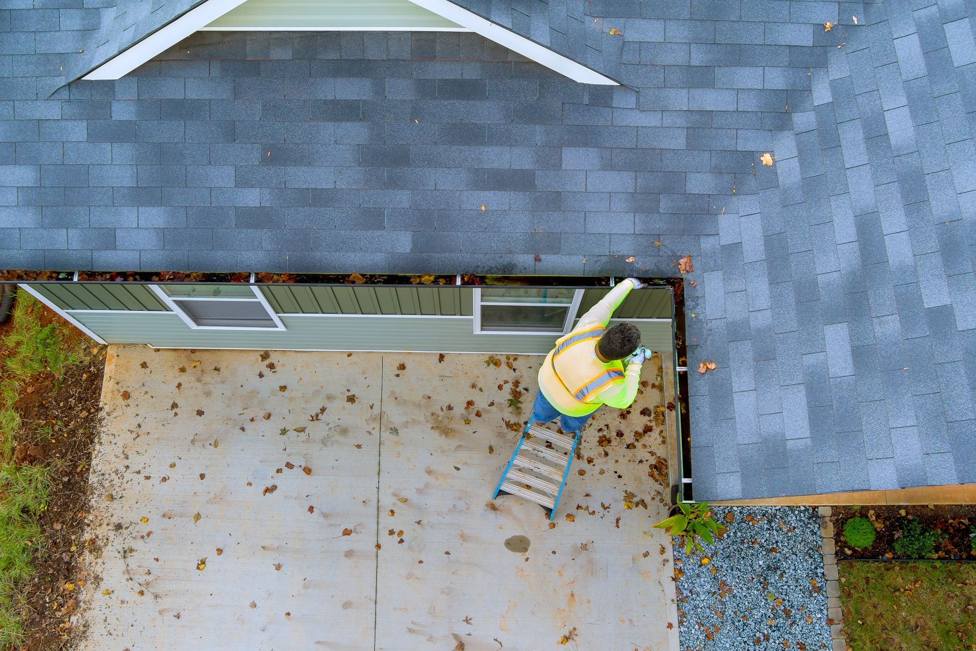 An aerial view of a man on a ladder cleaning the gutters of a house.