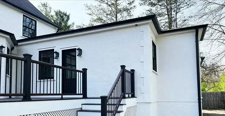 Une maison blanche avec une terrasse noire et des escaliers qui y mènent.