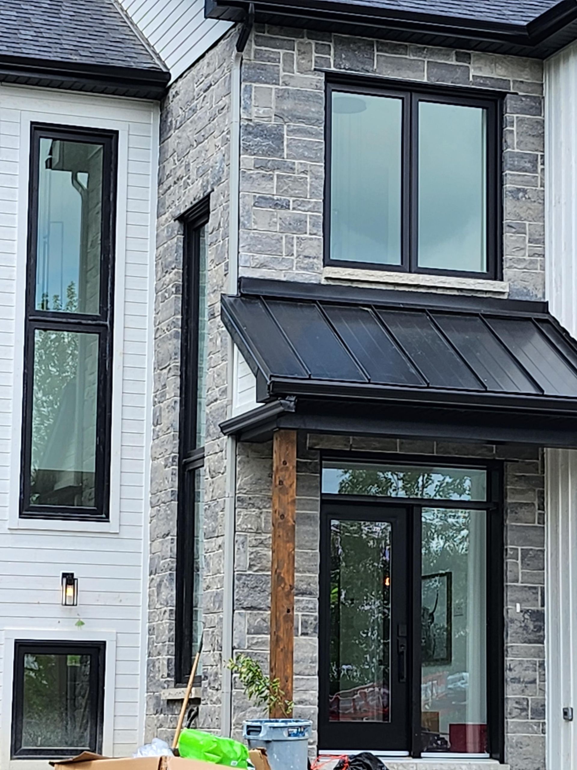 Extérieur d'une maison moderne avec un revêtement en pierre et blanc, des fenêtres à cadre noir et un toit en métal noir.