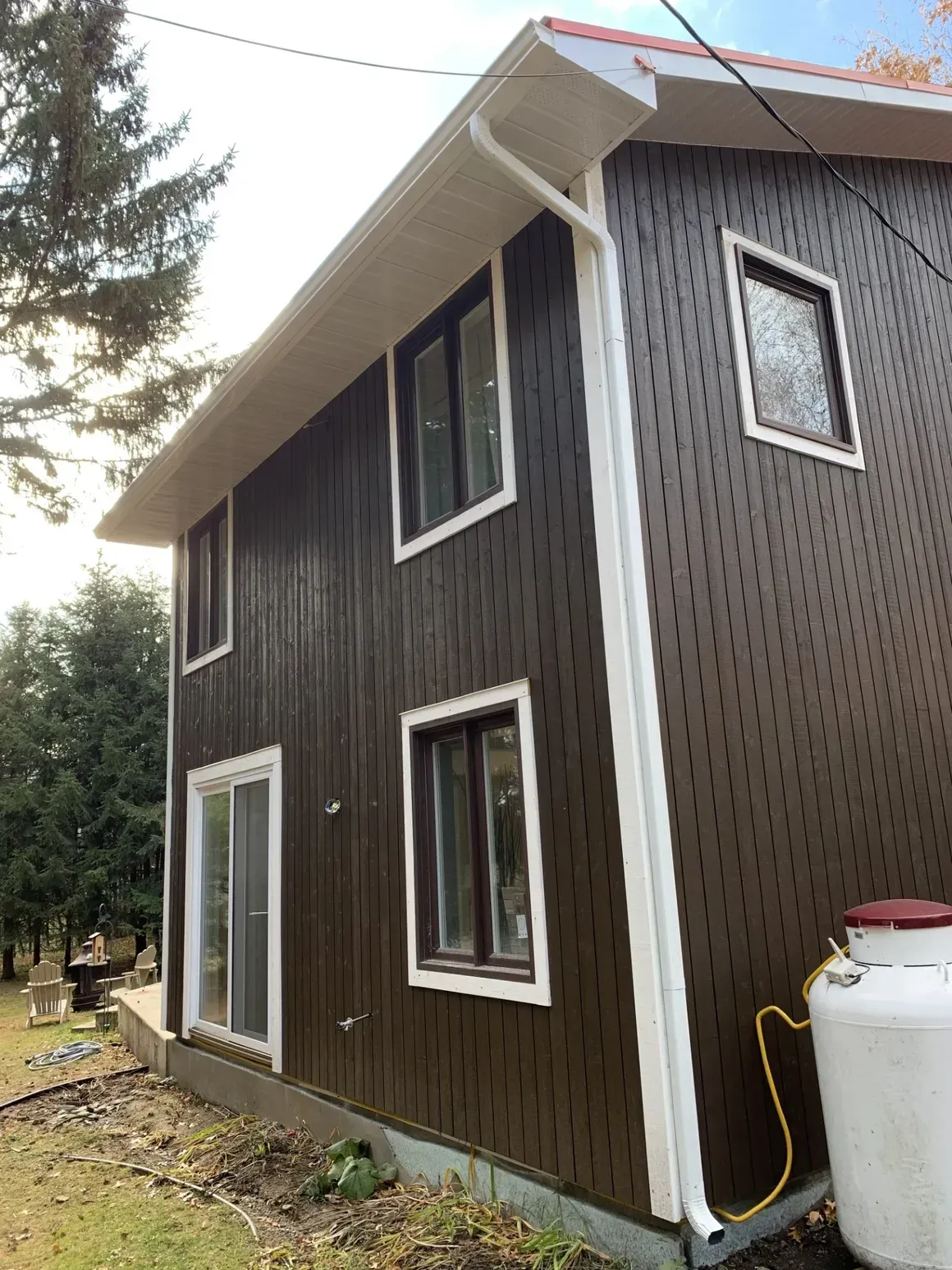 Une maison avec un revêtement marron et des garnitures blanches est située au sommet d'un champ vert luxuriant.