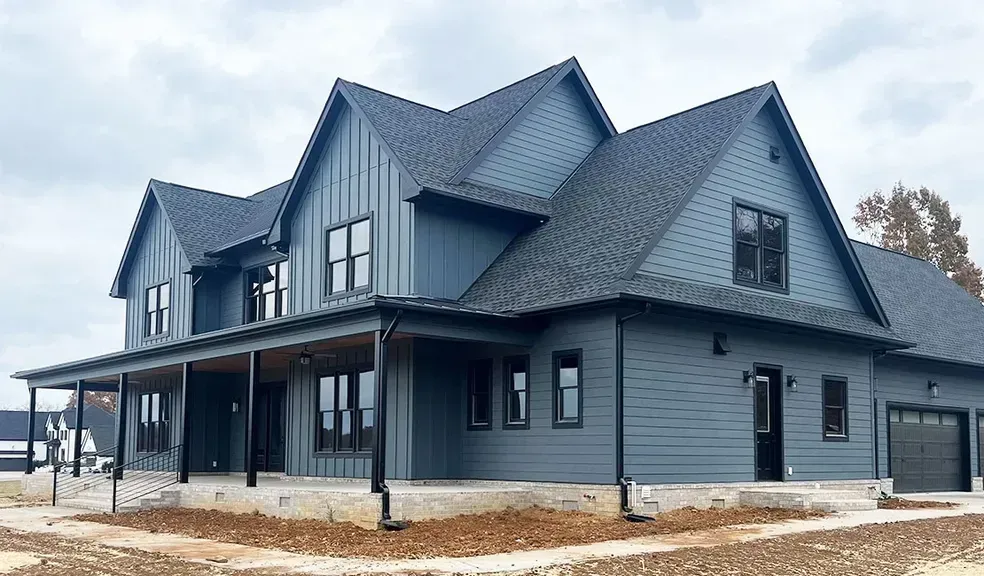 Une grande maison bleue avec un toit noir et un porche.