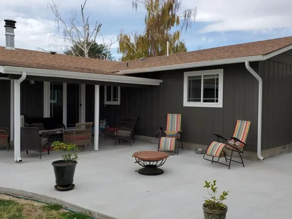Un patio avec des chaises, une table et un foyer devant une maison.