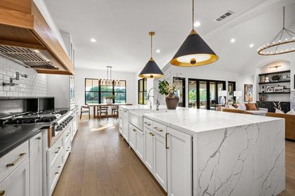 Spacious modern kitchen with white cabinets, marble island, and pendant lights.