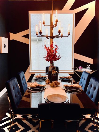 Dining room with black walls, gold geometric design, dark velvet chairs, and table set for a meal.