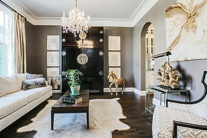 Living room with dark walls, white sofa, cowhide rug, black door, crystal chandelier.