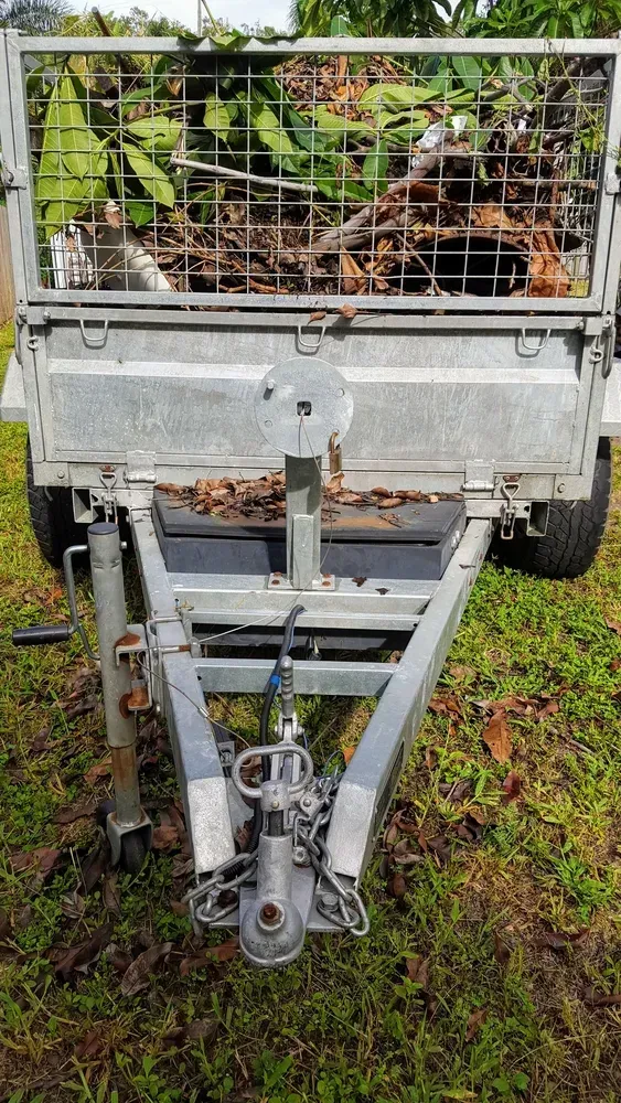 A utility trailer loaded with yard waste, parked outdoors on grass. — Resolute Home Services In Crows Nest, QLD
