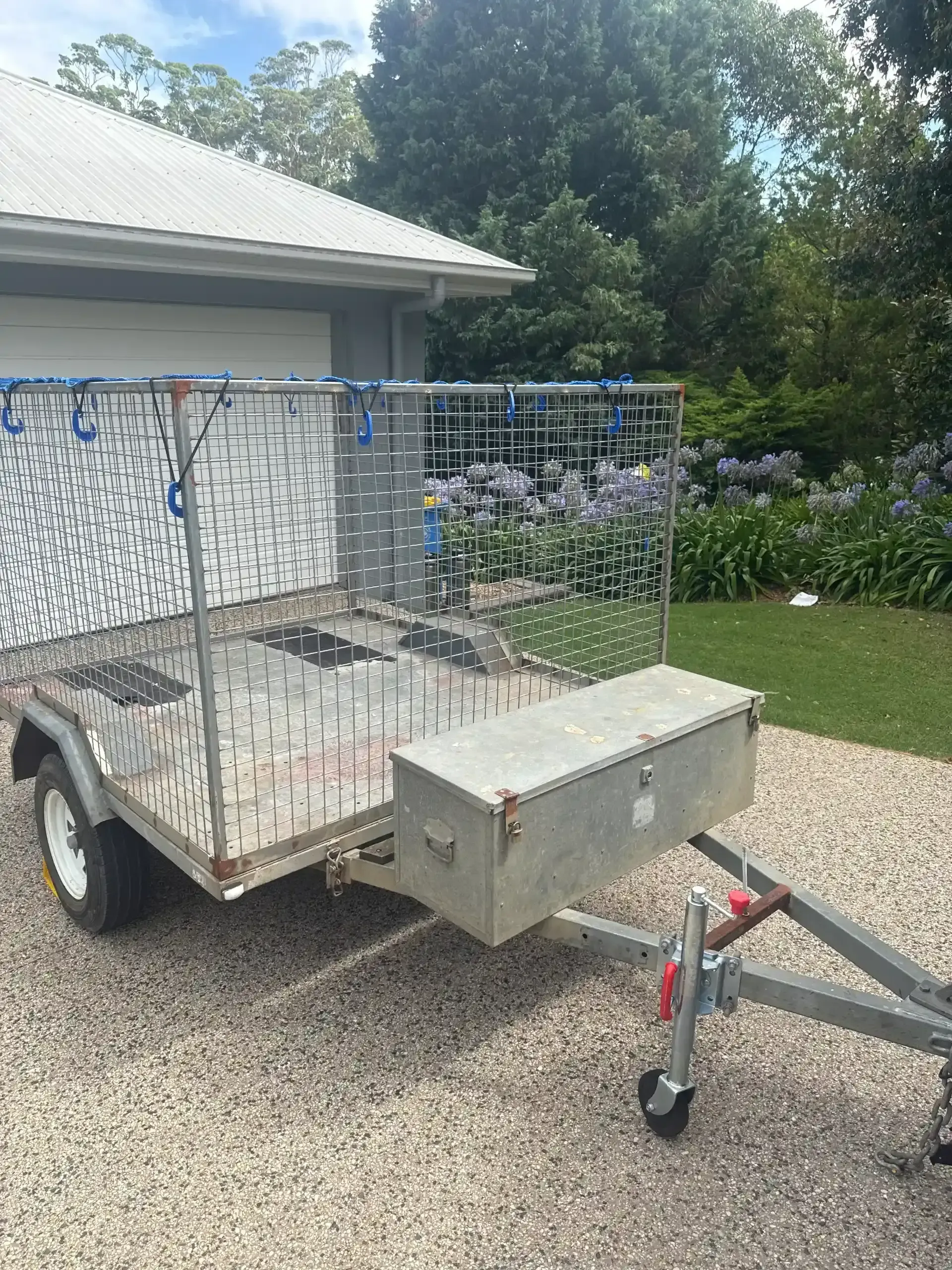 A small, aluminum utility trailer with a cage, tool box, and wheels parked on gravel driveway. — Resolute Home Services In Oakey, QLD