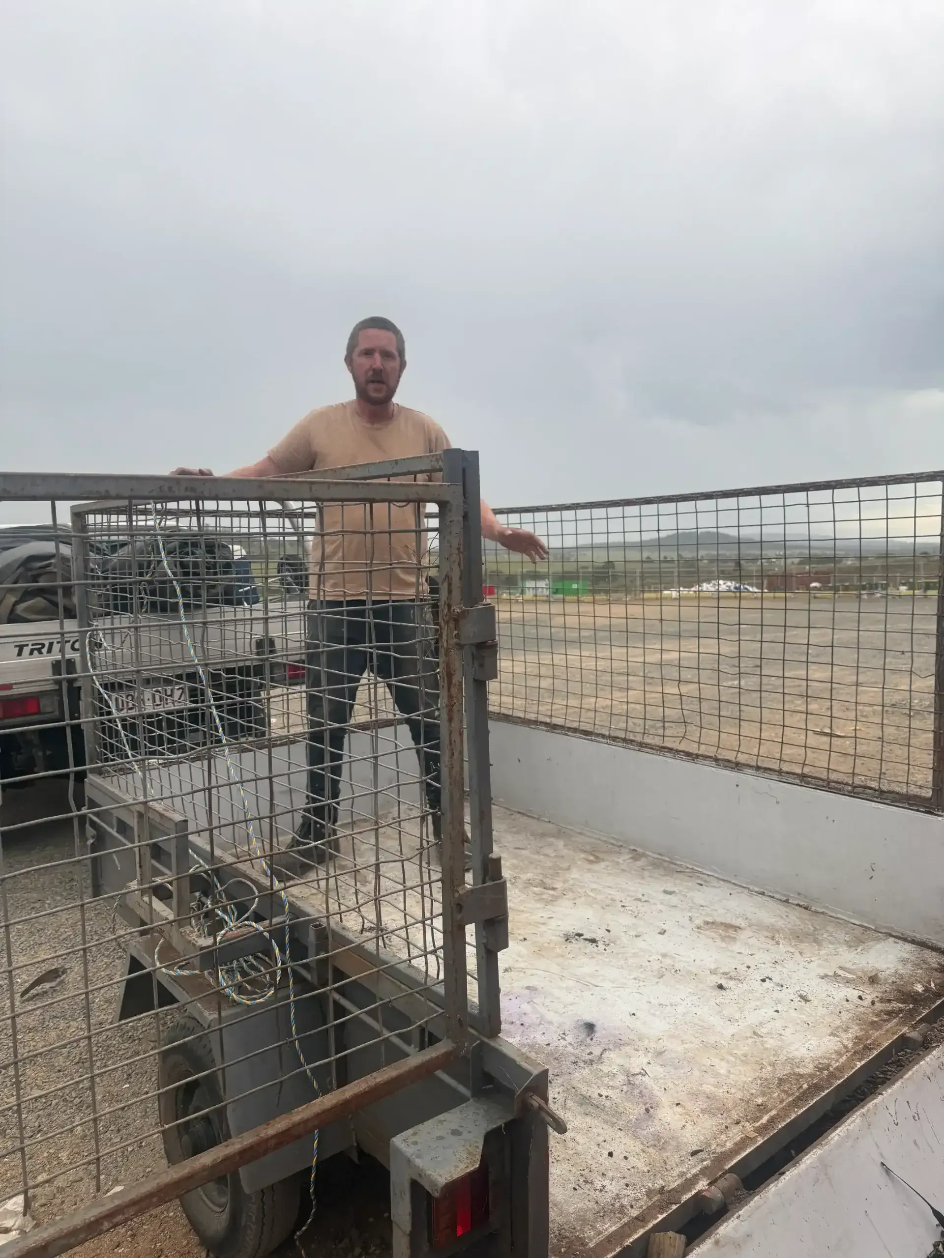 Man standing shirtless in a trailer with a metal cage, overcast sky. — Resolute Home Services In Gatton, QLD