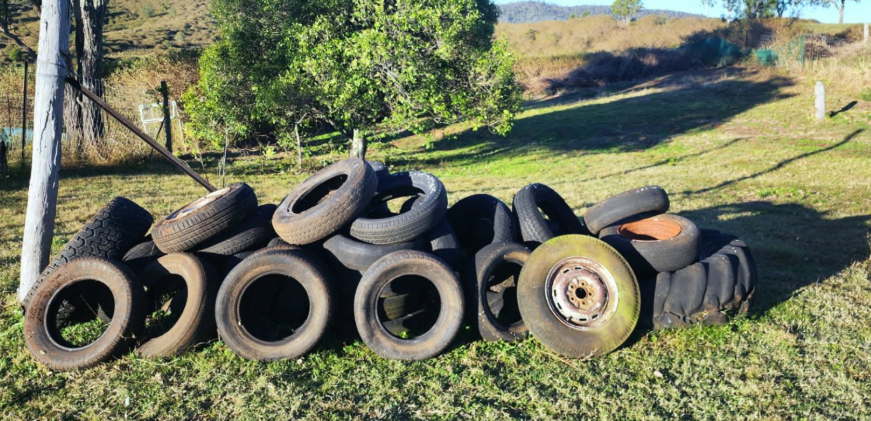 Pile of discarded tires on a grassy hill, with trees and a distant landscape.