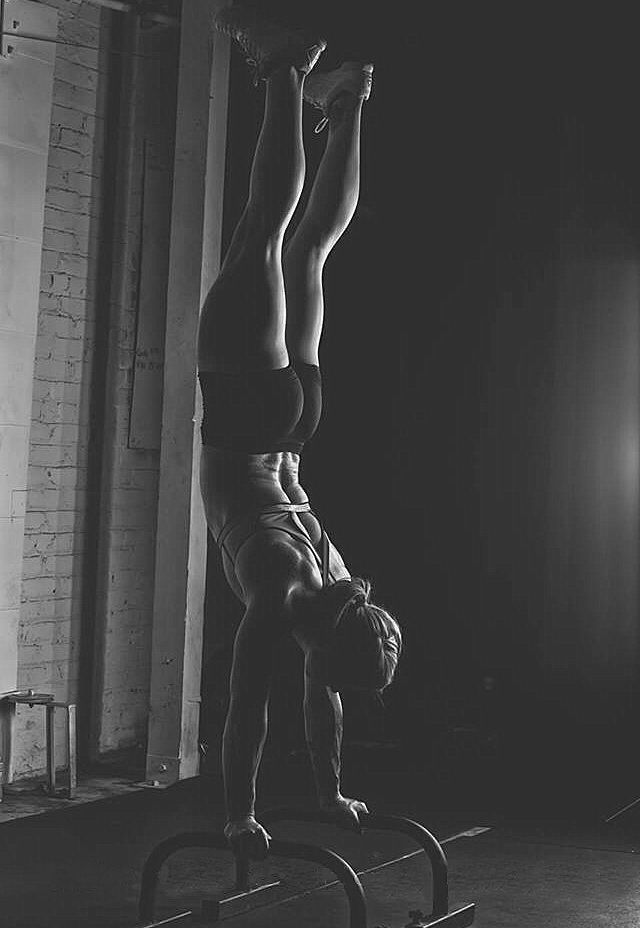 Woman doing a handstand on parallel bars in a dark gym.