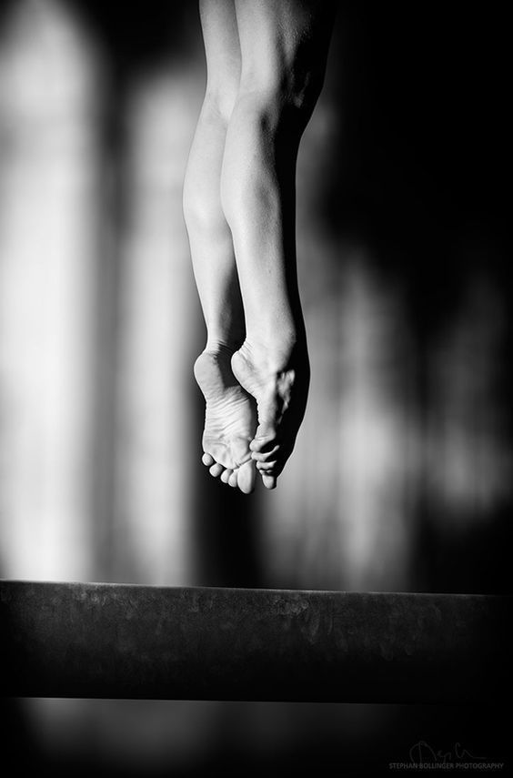 Gymnast's feet and legs, in black and white, over a balance beam.