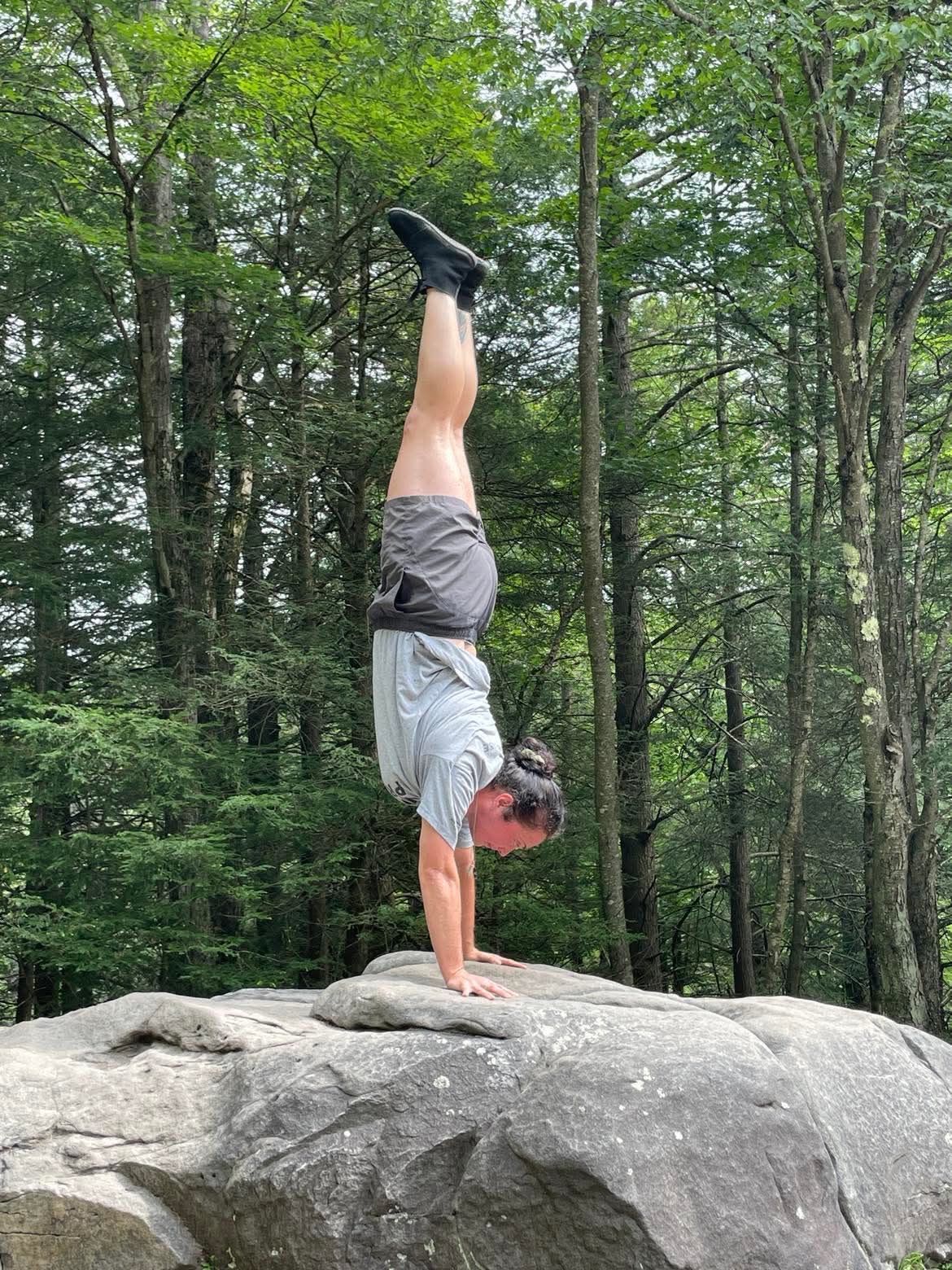 Person doing a handstand on a boulder in a forest.