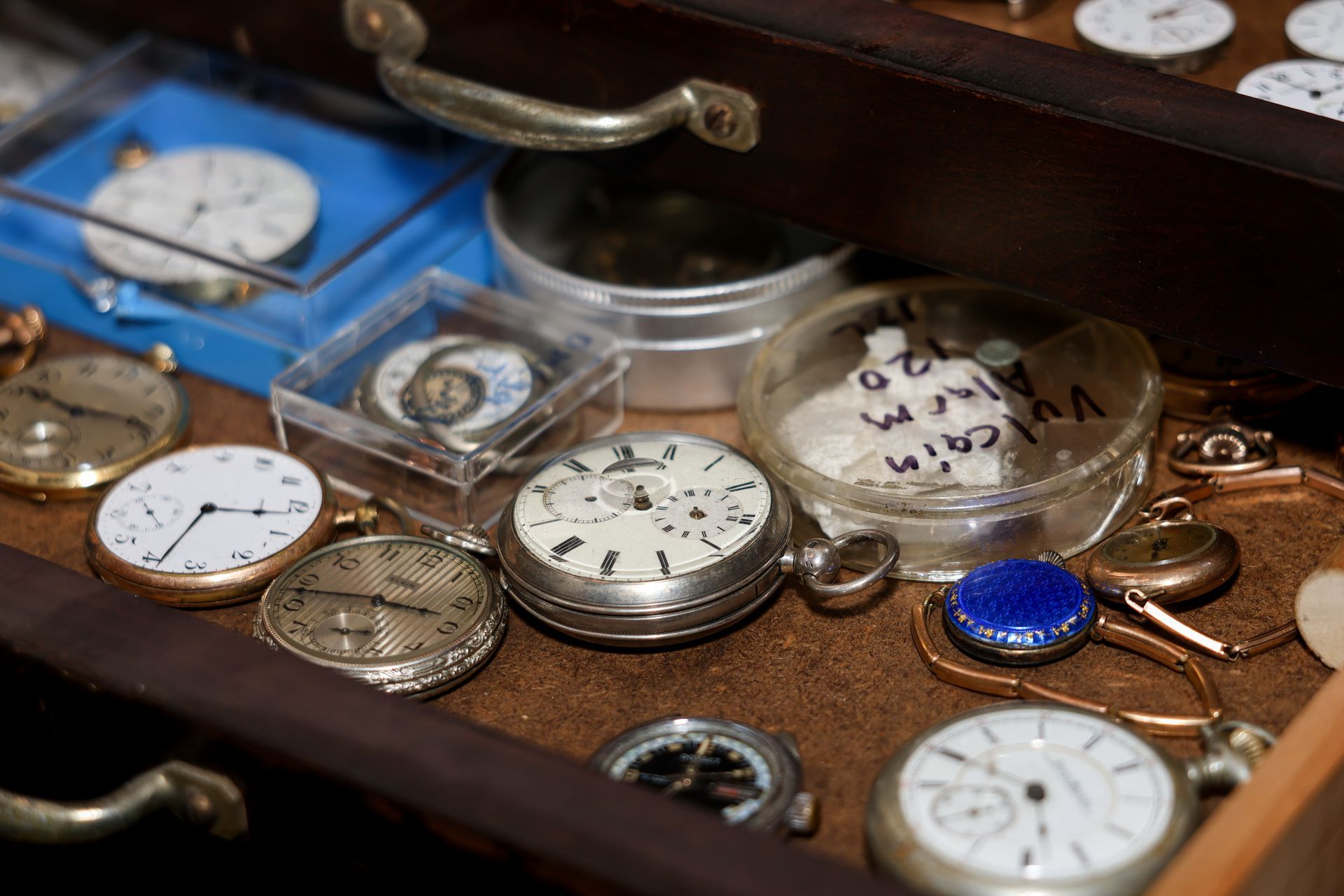 Close-up of an open wooden drawer filled with various antique pocket watches and watch components.