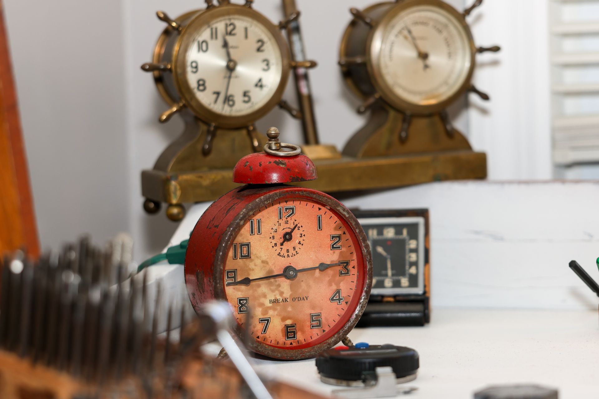 Red alarm clock in focus, with two antique ship wheel clocks in the background.