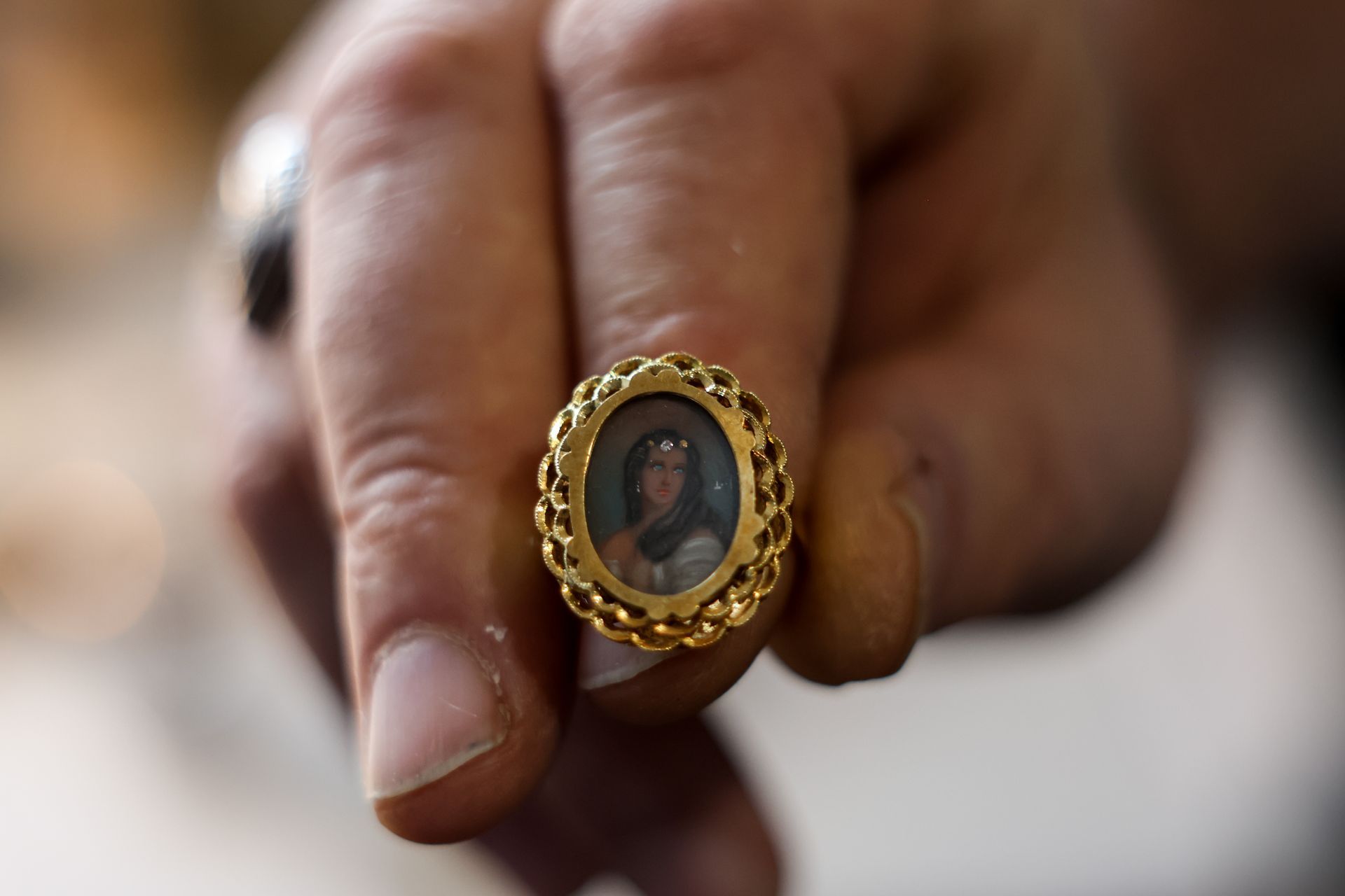 Gold ring with a portrait of a person held in a hand.