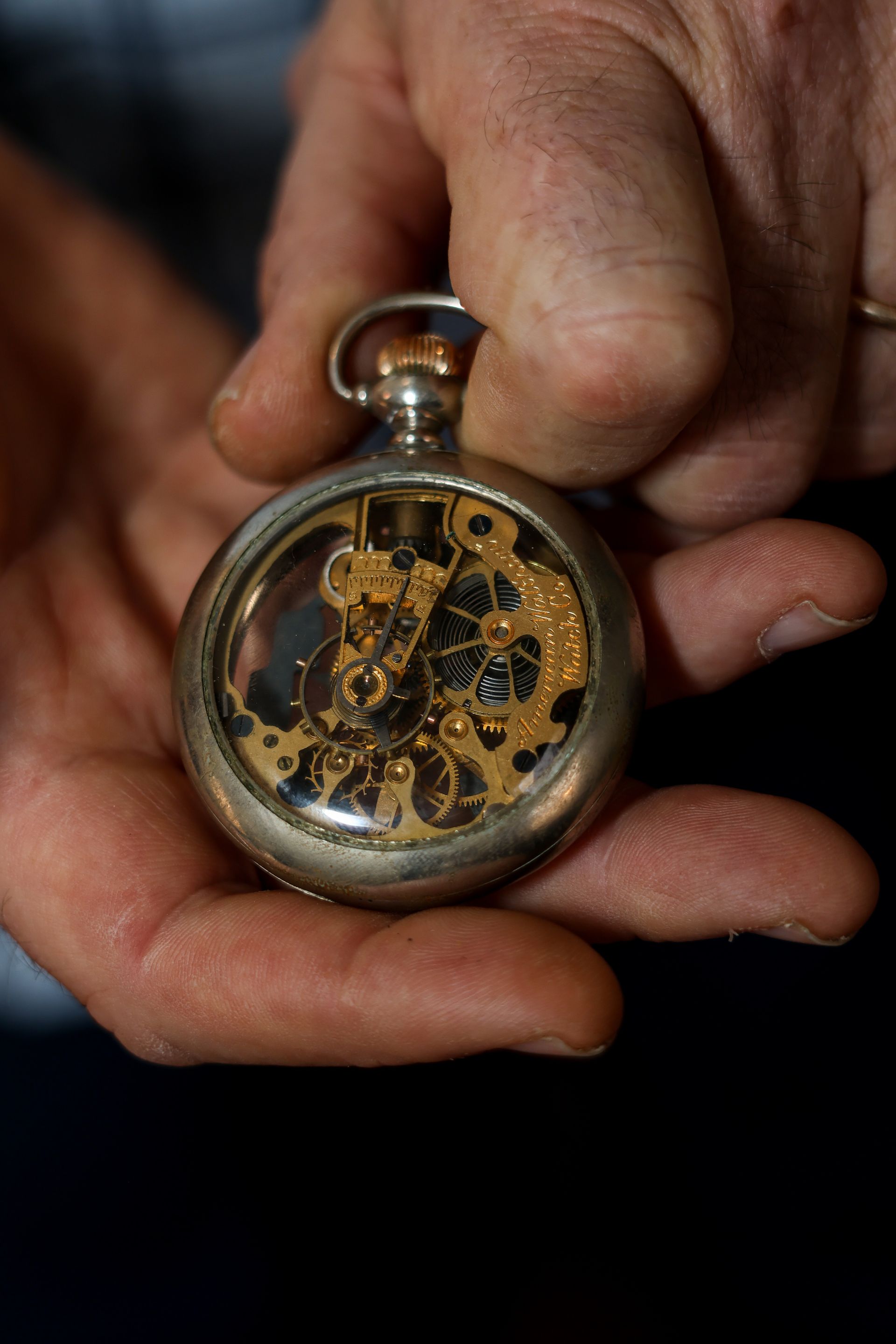 Silver pocket watch with visible gears, held in two hands.