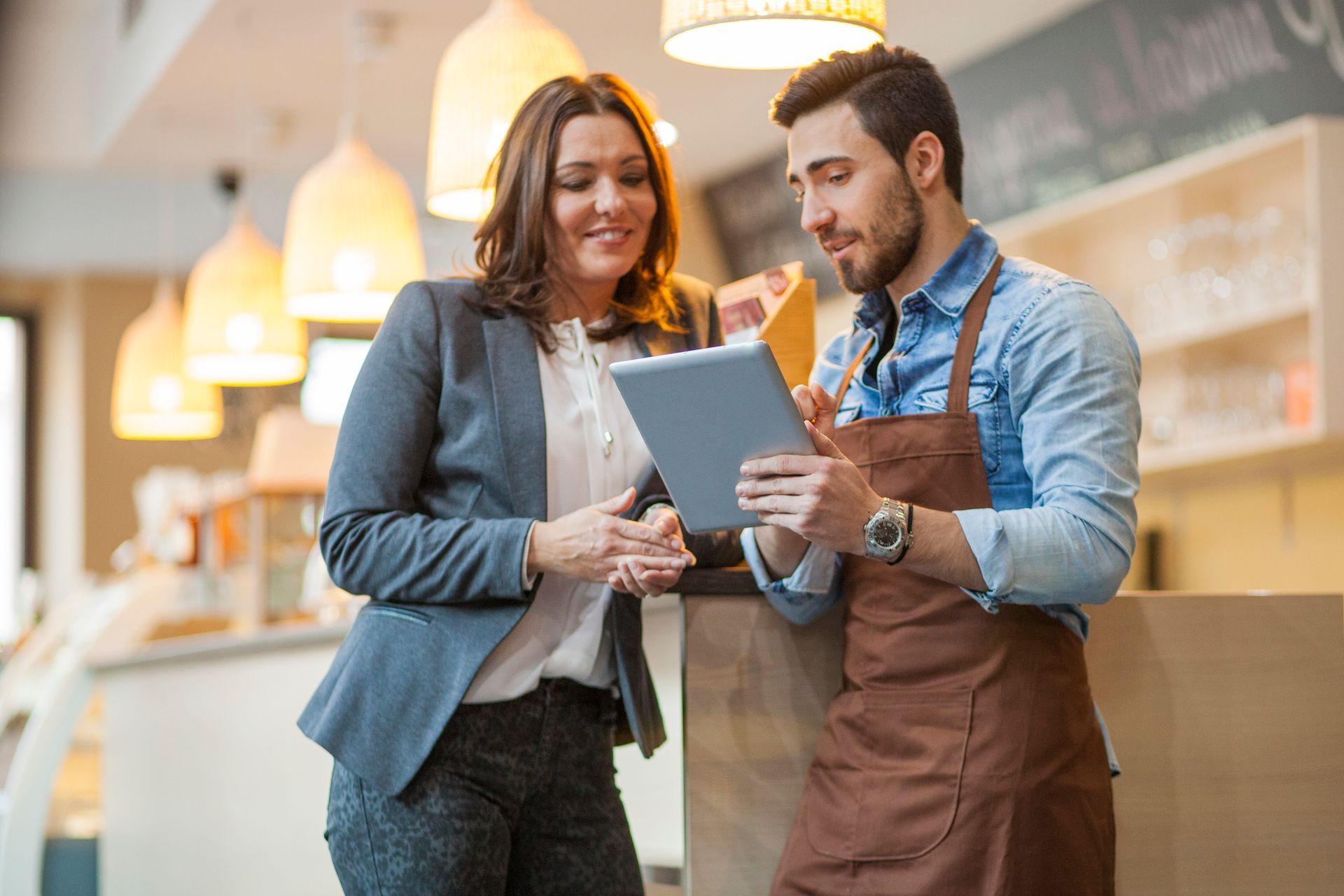 A man and a woman are looking at a tablet in a restaurant.