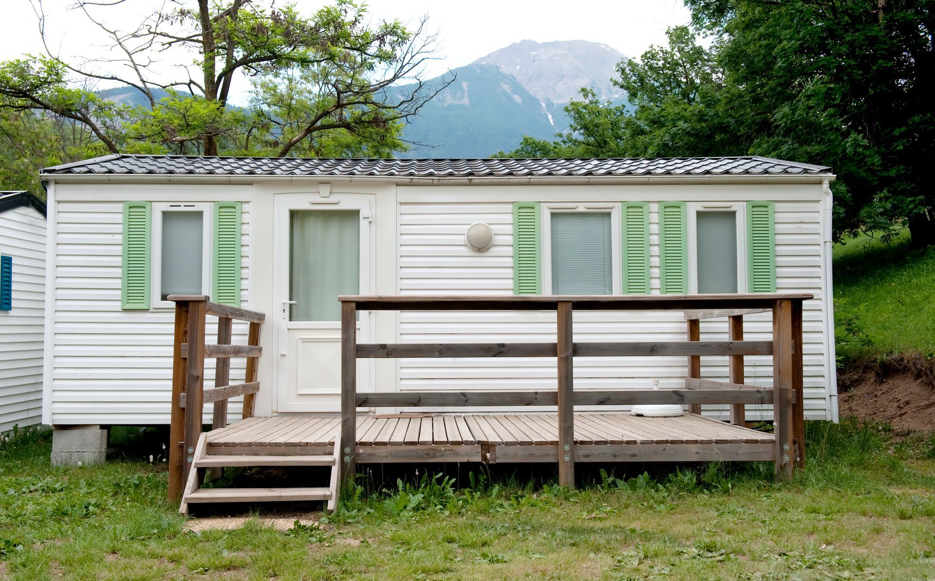 A white mobile home with green shutters and stairs