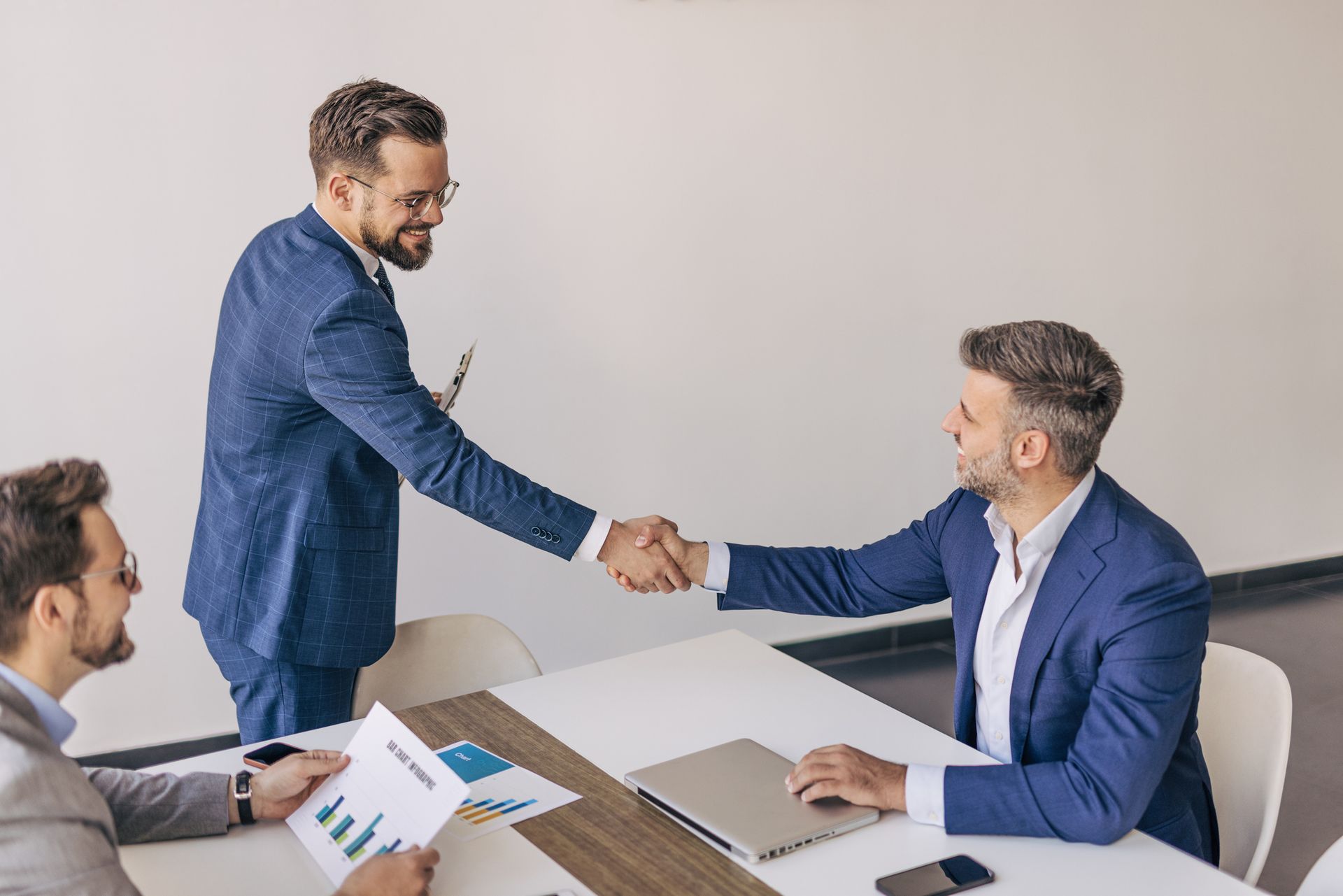 Two men are shaking hands while sitting at a table.