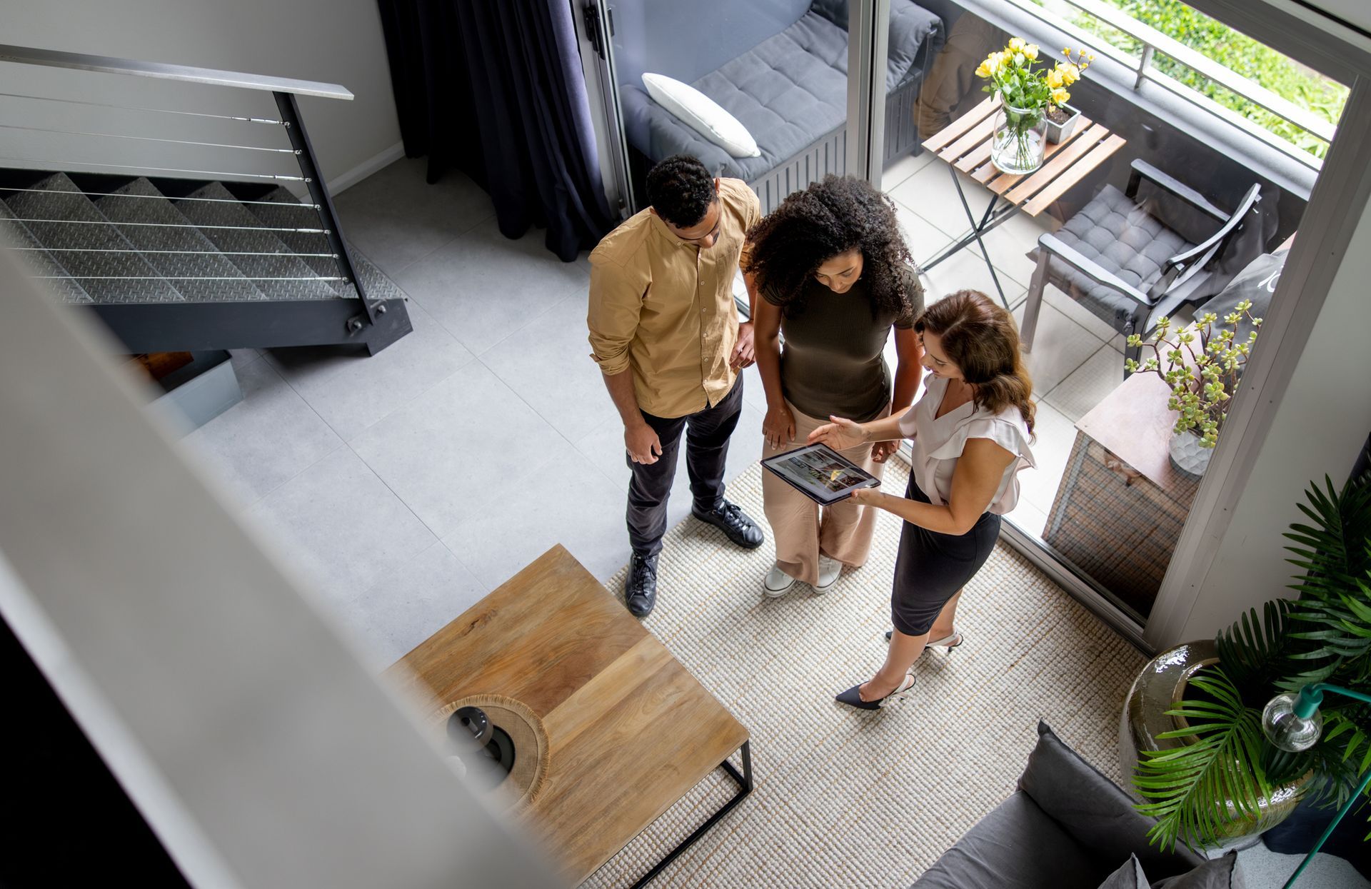 A group of people are standing in a living room looking at a tablet.