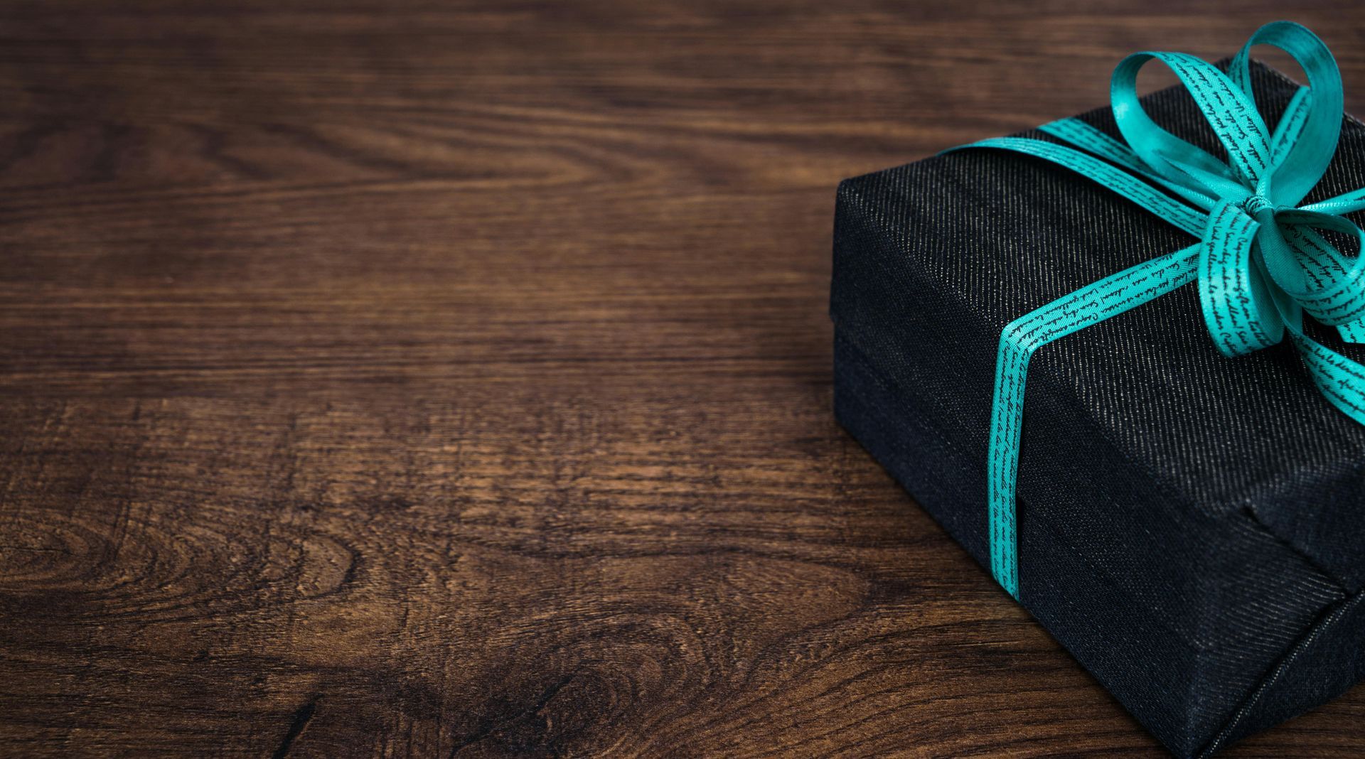 A black gift box with a blue ribbon on a wooden table.