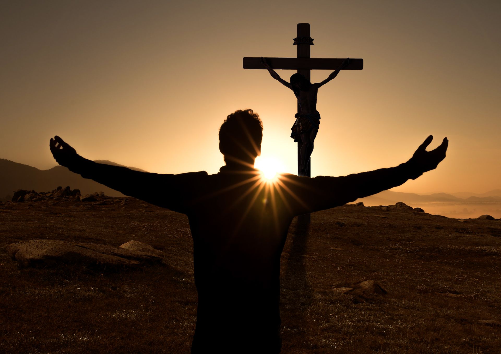 A man stands in front of a cross with his arms outstretched