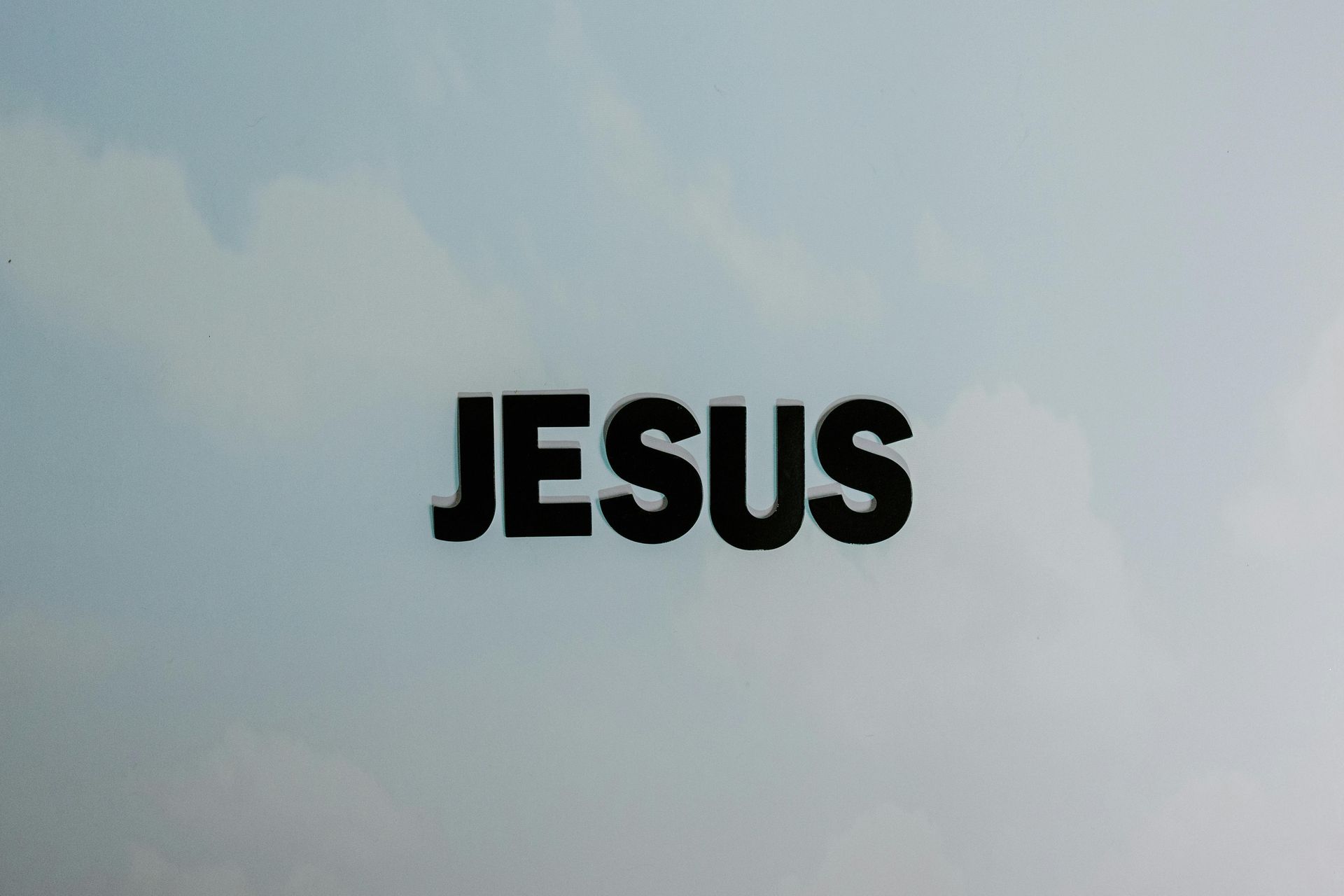 The word Jesus is against a cloudy sky.