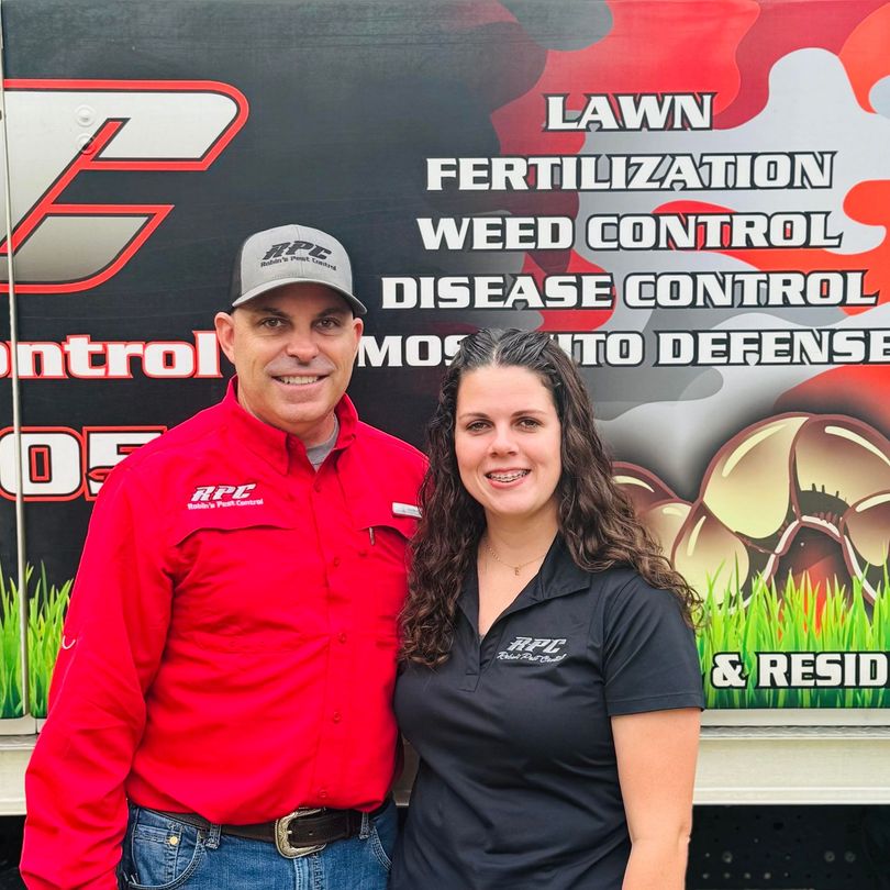 A man and a woman are posing for a picture in front of a lawn fertilizer truck.