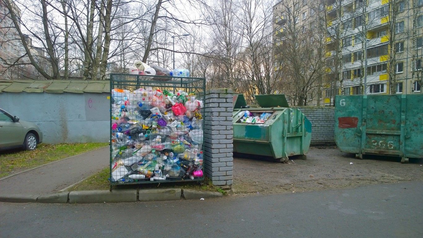Colorful compressed recycling bale beside green dumpsters in a gray outdoor lot