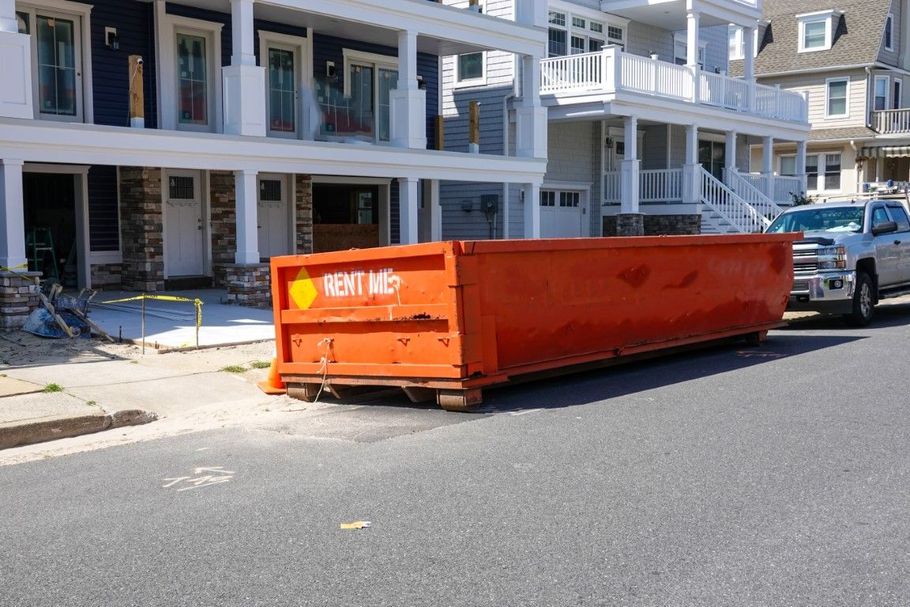 Orange construction dumpster on a residential street beside apartment buildings.