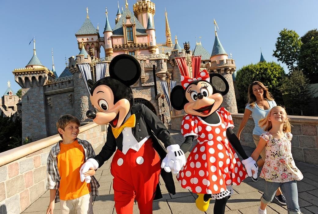 Mickey and Minnie Mouse with two children at Disneyland, walking in front of Sleeping Beauty Castle.