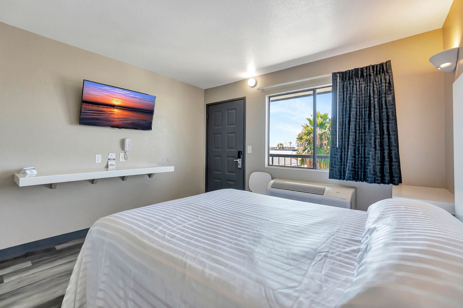 Bedroom interior with bed, TV on wall, window with curtains, and closed door.