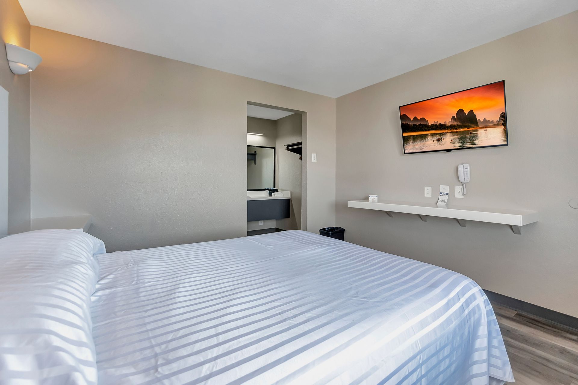 Bedroom with bed, television, and bathroom entrance. Neutral walls and flooring, simple decor.