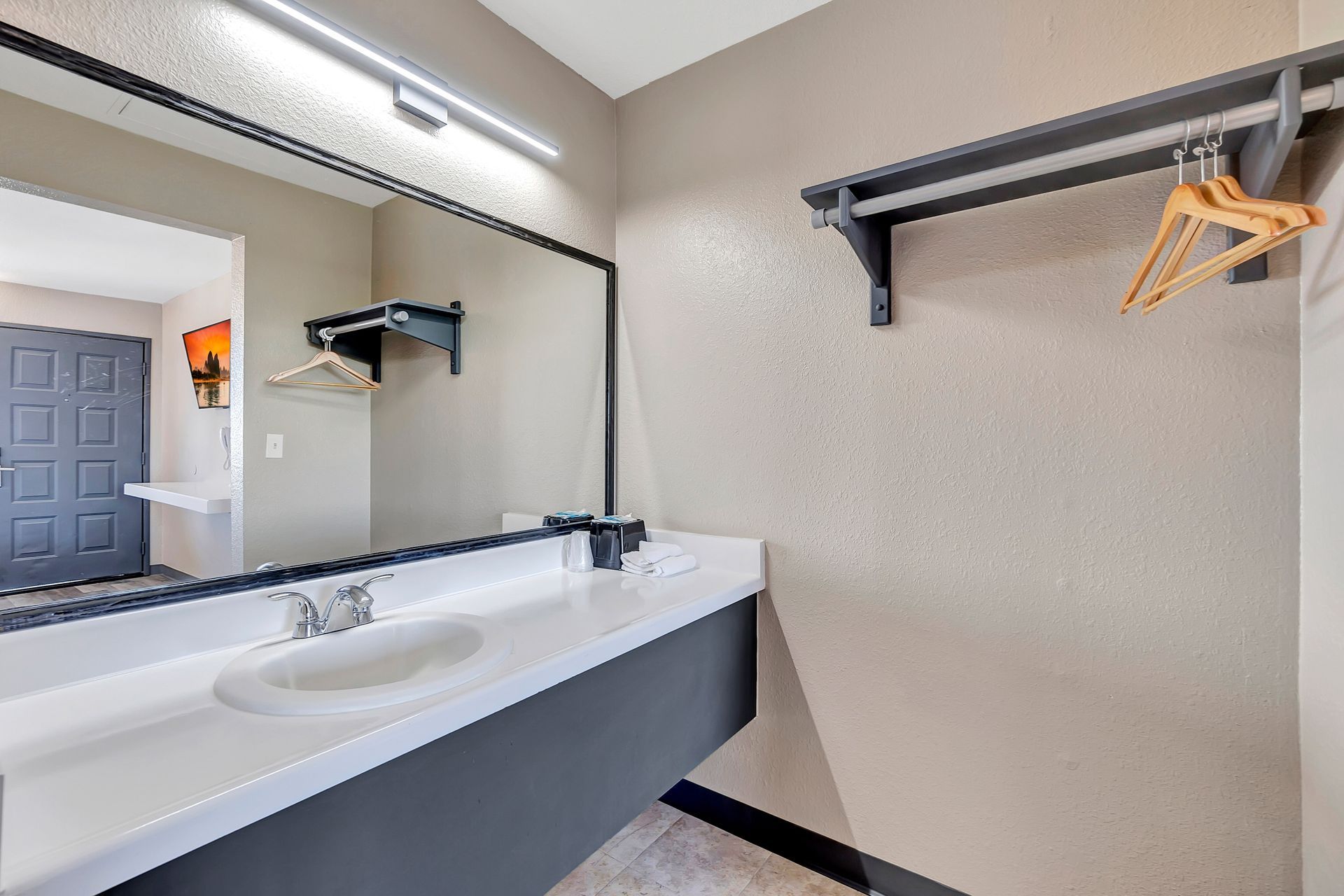 Bathroom with large mirror over a sink, rack with hangers, and doorway. Beige walls and gray accents.