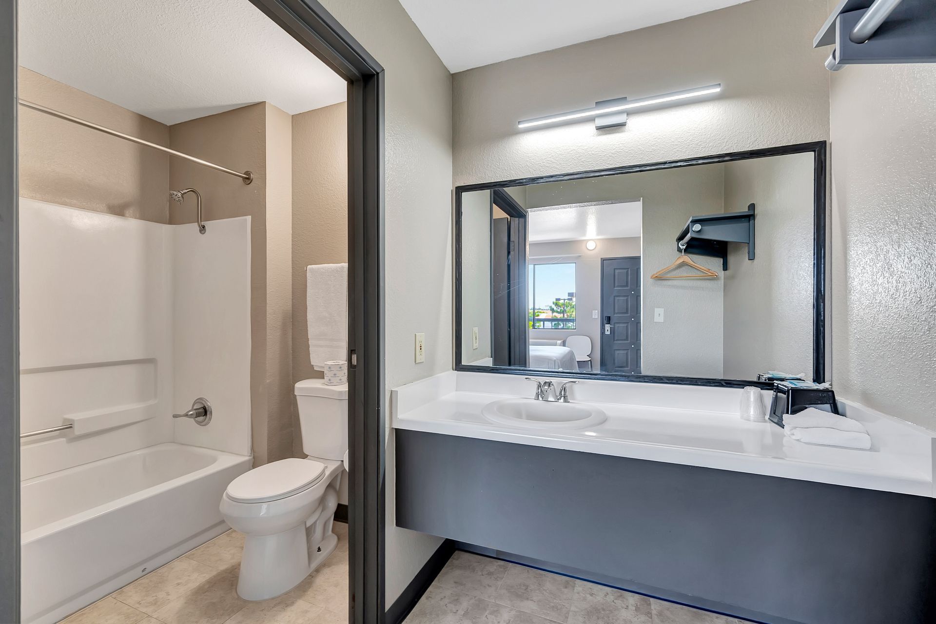 Bathroom with white tub, toilet, and vanity with mirror. Gray and white color scheme.