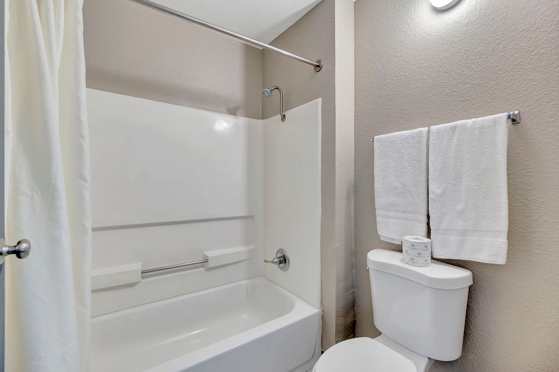 Bathroom with white tub/shower combo, toilet, and two white towels. Light gray walls.