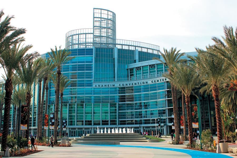 Anaheim Convention Center, a large teal-glass building with a tower, palm trees in the foreground.
