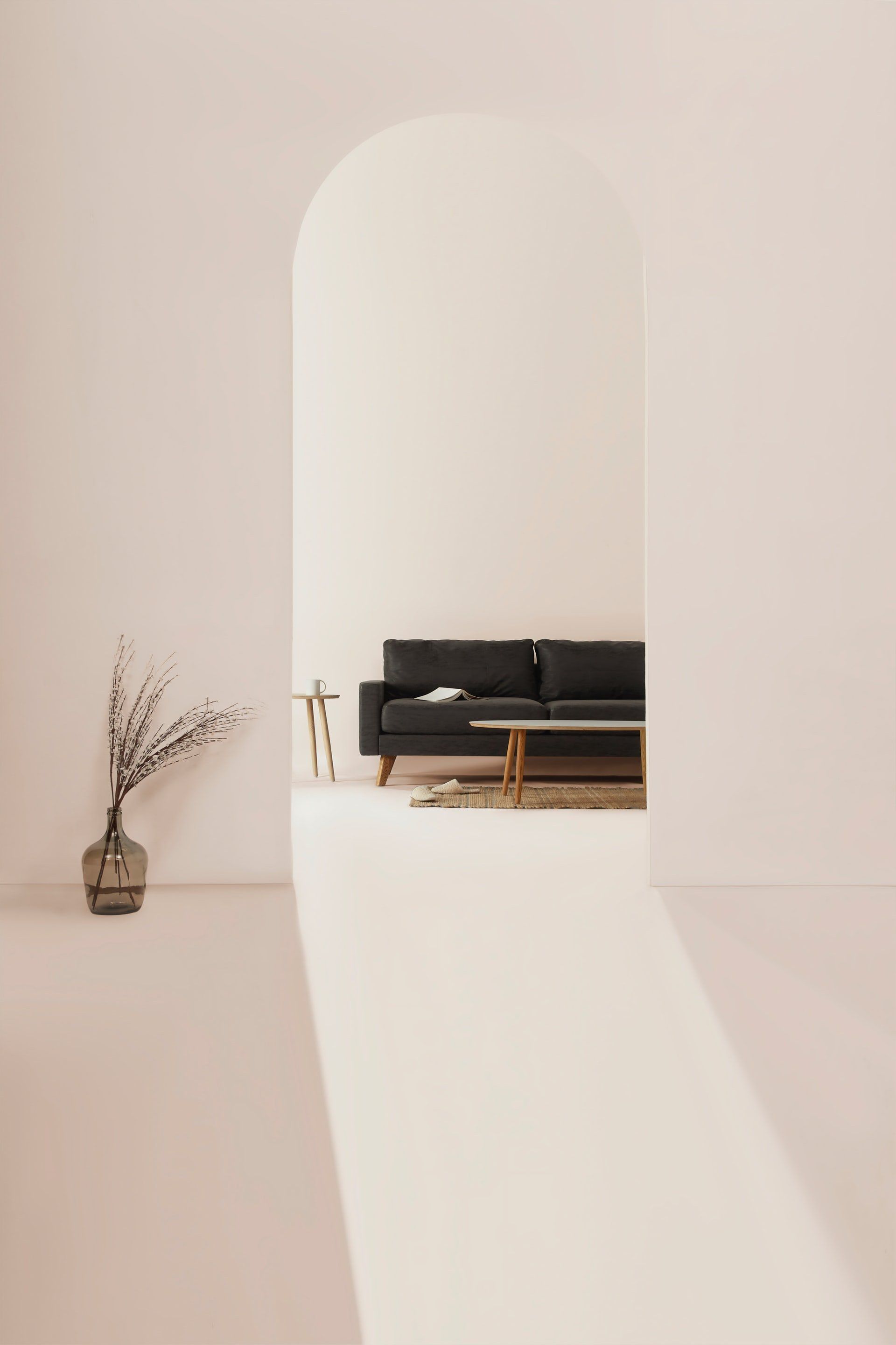 Archway reveals a black sofa, coffee table, and dried branches in a minimalist interior.