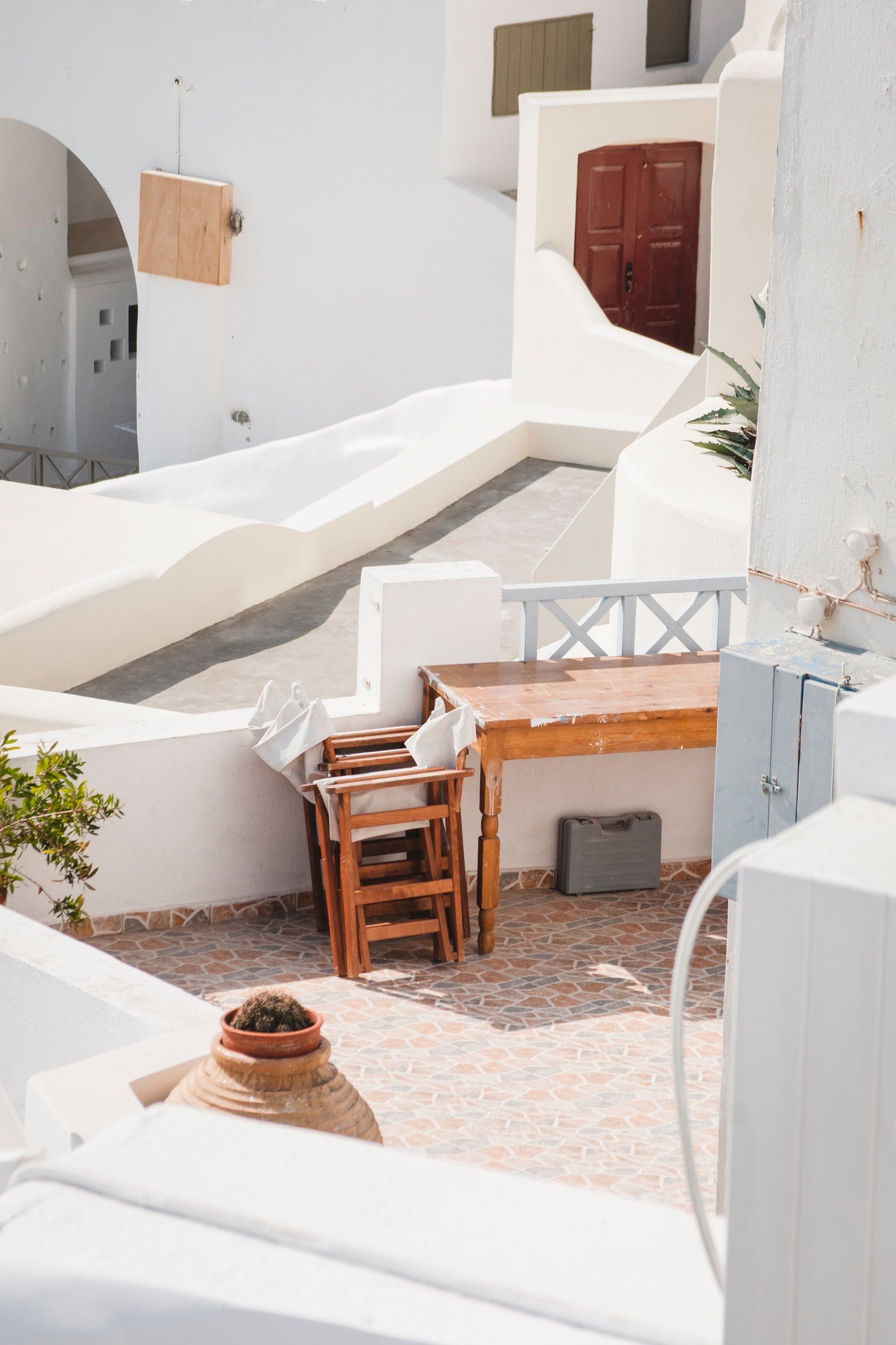 White buildings with stairs and a terrace. Wooden table and chairs are on the terrace.