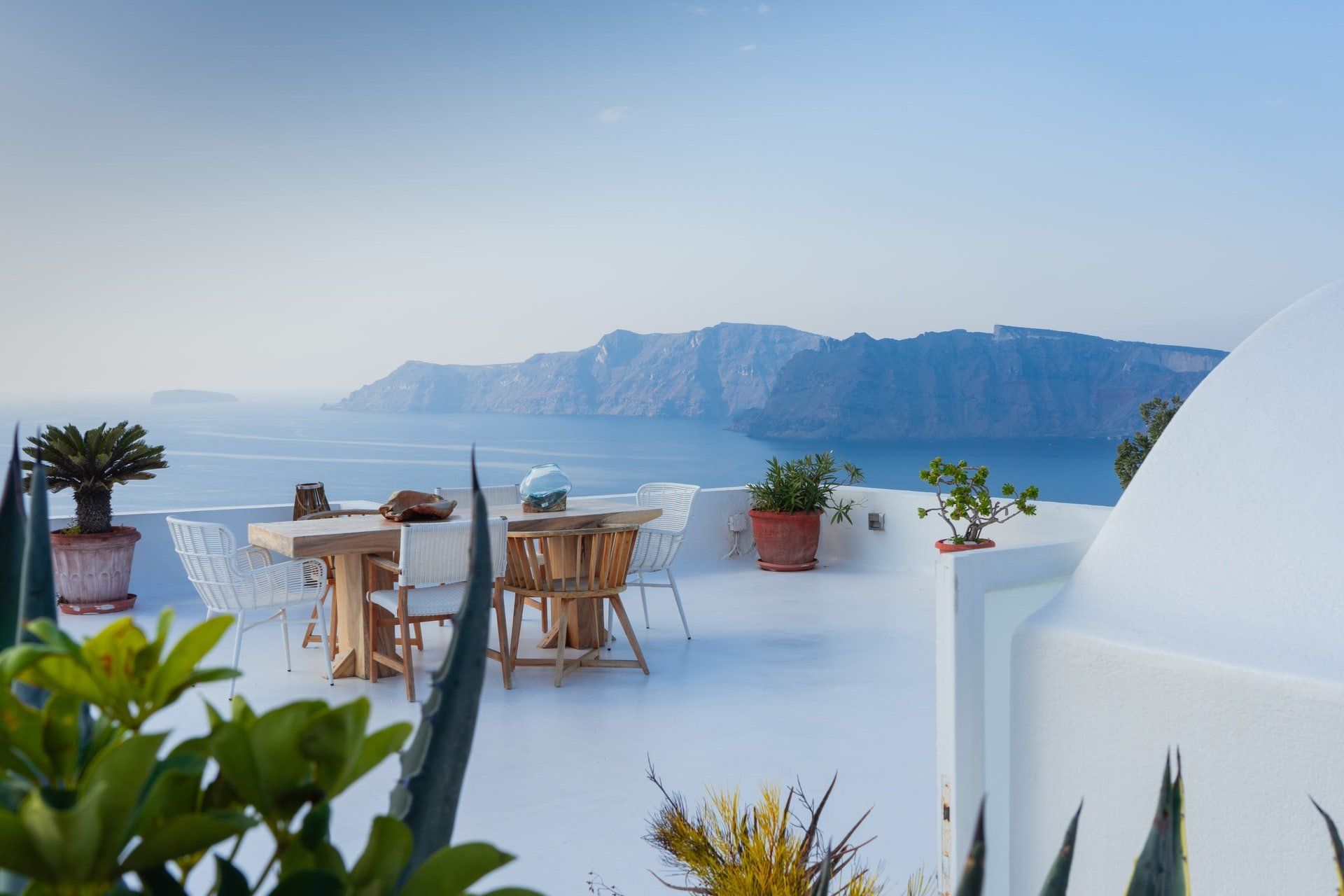 White patio with table and chairs, overlooking a blue sea and distant island.