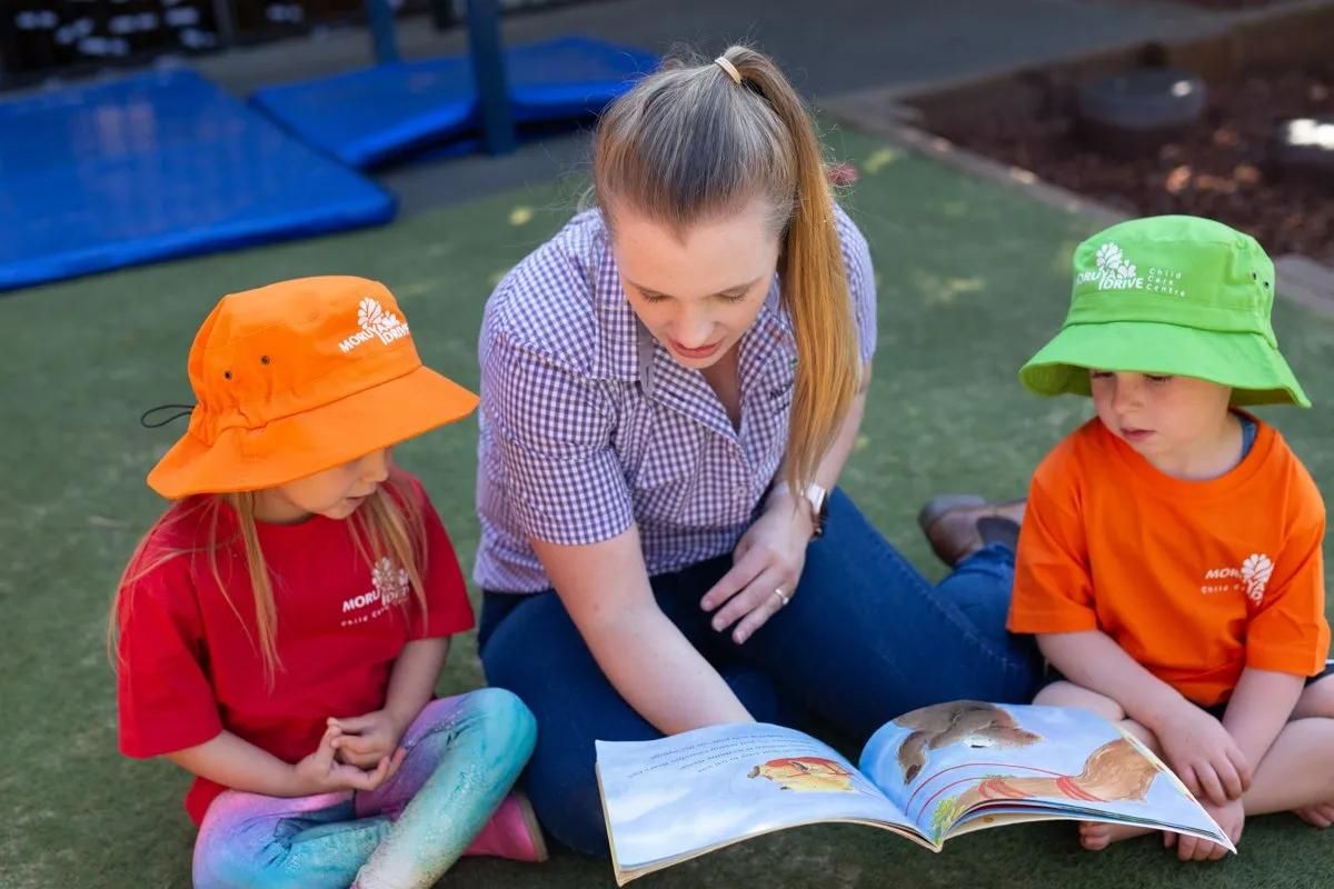 A Woman Is Reading A Book To Two Children — Moruya Drive Child Care Centre In Port Macquarie, NSW