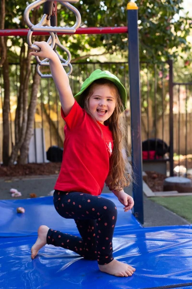 A Little Girl Is Kneeling On A Blue Mat In A Playground — Moruya Drive Child Care Centre In Port Macquarie, NSW