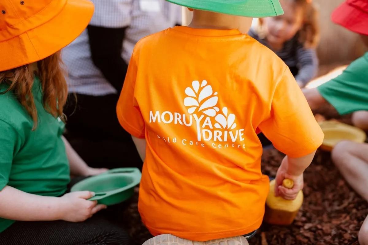A Child Wearing An Orange Shirt That Says Moruya Drive — Moruya Drive Child Care Centre In Port Macquarie, NSW